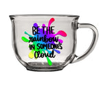 Clear glass mug with rainbow splatter and "be the rainbow in someone's cloud" text